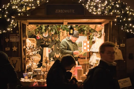 Man selling wooden crafts in decorated Christmas market stall with warm lights